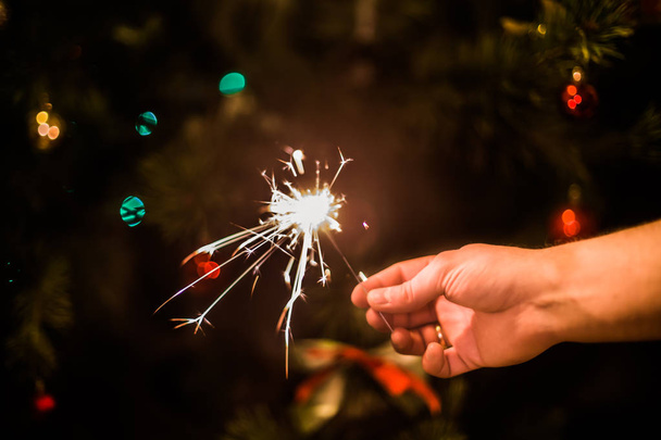 Hand with burning sparkler on xmas tree background - Photo, Image