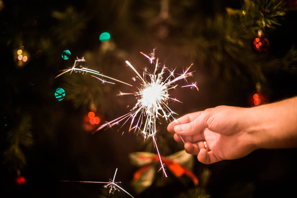 Ruka s hořící jiskru na pozadí vánočního stromu - Fotografie, Obrázek