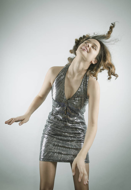 Vivacious dark-haired dancing in a brilliant miniskirt dress, studio portrait on gray. Copy space - Foto, afbeelding