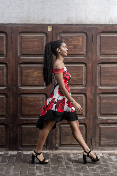 Kendine güvenen, renkli elbiseli, cadde boyunca yürüyen etnik bir kadın. - Fotoğraf, Görsel