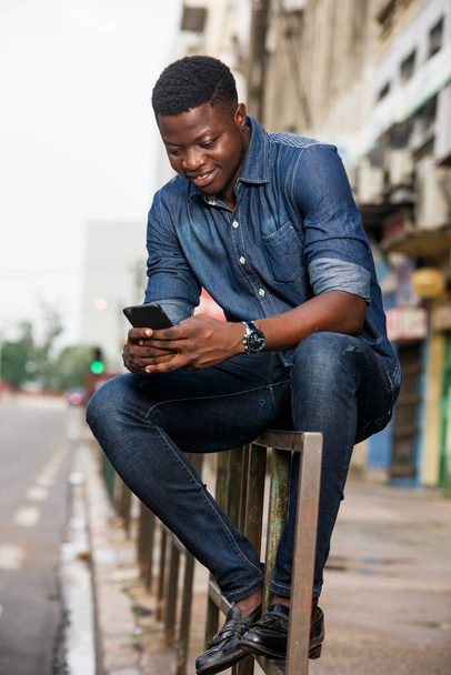 Portrait of a young man smiling a mobile phone in the street - Foto, Imagem