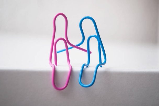 closeup of two paperclips sitting on white desk - love concept - 写真・画像