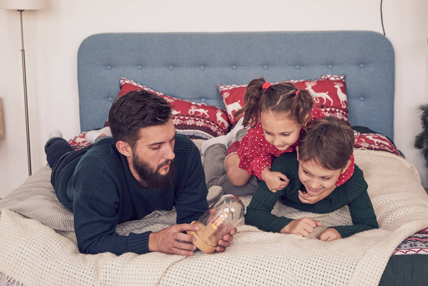 Fiatal család két gyerekkel otthon az ágyban. A szülők gyermekekkel pihennek az ágyban egy napsütéses reggelen. Boldog család otthon. Egy nagy család portréja fekszik az ágyon.. - Fotó, kép