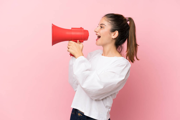 Young brunette girl over isolated pink background shouting through a megaphone - Foto, afbeelding