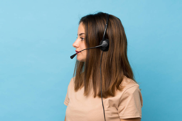 Young brunette girl over isolated blue background working with headset - Photo, Image