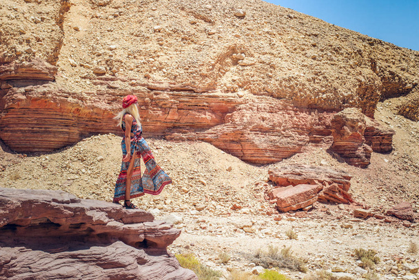 θέτοντας πρότυπο ευρωπαϊκή λευκή γυναίκα σε μακρύ φόρεμα μόδας κομψή φωτογραφία στο ισραηλινό φαράγγι της ερήμου ξηρή άμμος πέτρα βραχώδες τοπίο άγρια γραφικό περιβάλλον   - Φωτογραφία, εικόνα