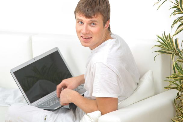 gülümseyen genç adam evde dizüstü bilgisayar üzerinde çalışan - Fotoğraf, Görsel