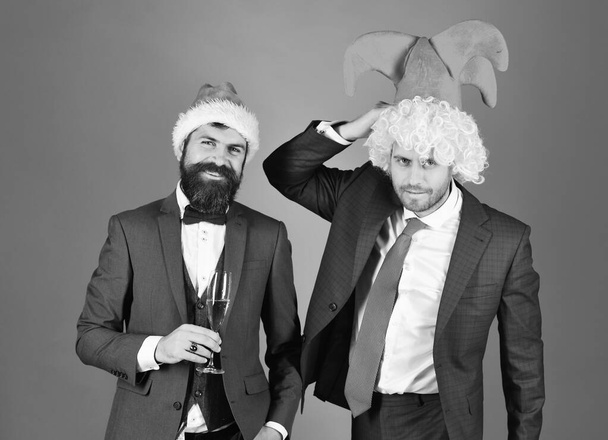 Men in smart suits, Santa and jester hats on red - 写真・画像
