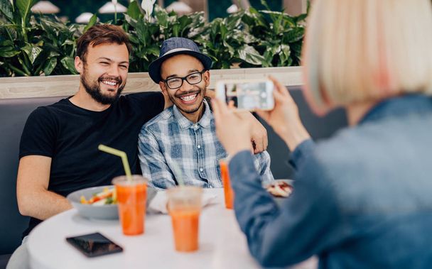 Woman taking photo of diverse friends in cafe - Photo, image
