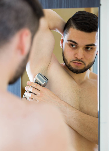 Man shaving armpit with trimmer - 写真・画像
