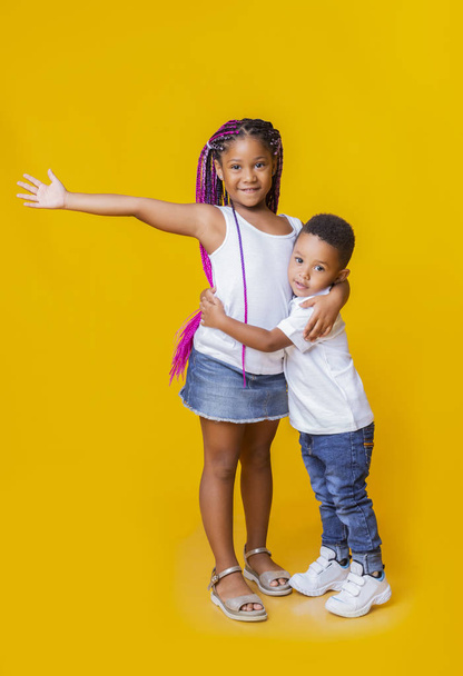 Kleine zwarte broers en zussen samen poseren op gele achtergrond in de studio - Foto, afbeelding