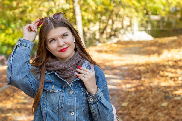 Una joven escucha música en un parque de otoño. Paseo de otoño en el parque. Sueños y música
. - Foto, Imagen