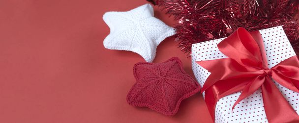 Christmas banner with gift box, tinsel, and knitted stars. Gift concept for needlewoman on a red background - Фото, зображення