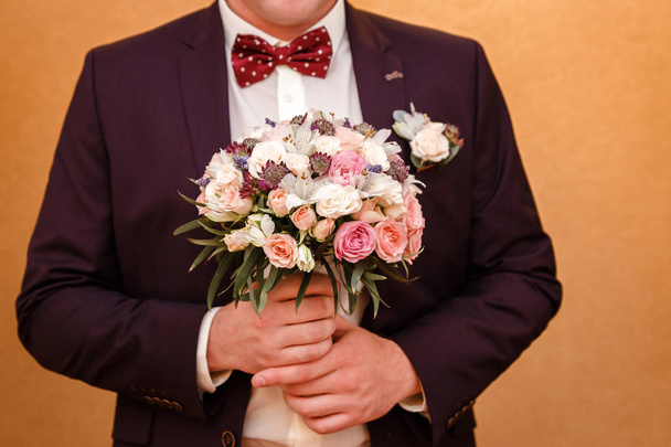 a man in a jacket and bow tie holding a wedding bouquet - Fotó, kép