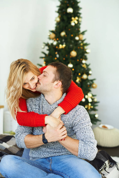 Romantic couple in love embracing, kissing sitting, on the bed near the Xmas tree at home. - Foto, imagen