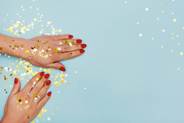 Woman hands with red manicure on blue background with golden stars sprinkles. - Zdjęcie, obraz