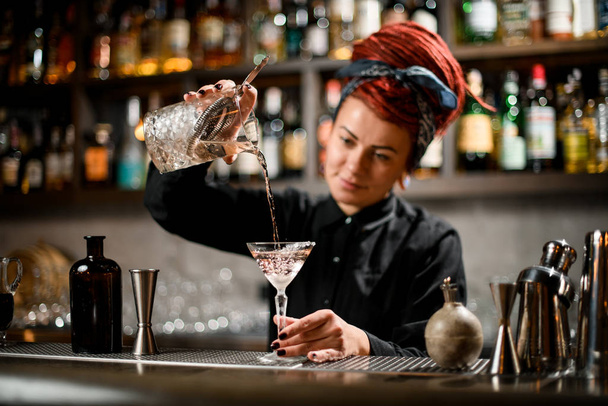 Bartender pours drink using glass with strainer inside - Foto, Imagen