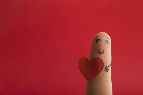 Walentynki zakochują się w koncepcji miłości. Malowane szczęśliwe śmieszne palce smiley trzymając czerwone serce na czerwonym tle z miejsca na tekst reklam - Zdjęcie, obraz