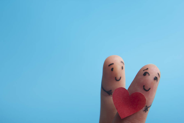День Святого Валентина в любви концепции. Раскрашенные счастливые пальцы улыбаются в любви с красным сердцем на синем фоне
 - Фото, изображение