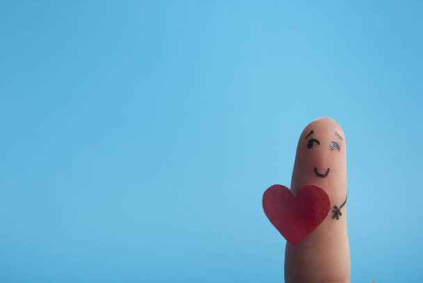Valentýn se zamiluje do konceptu. Malované šťastné prsty smajlík v lásce s červeným srdcem proti modrému pozadí - Fotografie, Obrázek