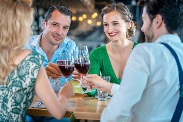 Мужчины и женщины тосты с красным вином в ресторане
 - Фото, изображение