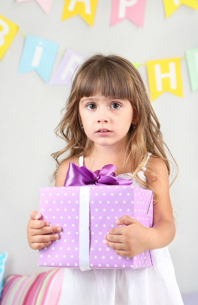Little girl with gift in room on grey wall background - Foto, immagini