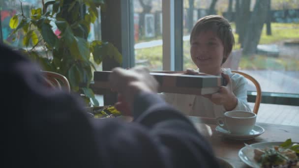 Jongen geeft een cadeau aan zijn vader in een café - Video
