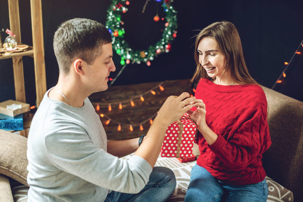 Erkek koca karısına sürpriz bir hediye kutusu verir. Evli çift Noel 'i ve yeni yılı ev ortamında kutluyor - Fotoğraf, Görsel