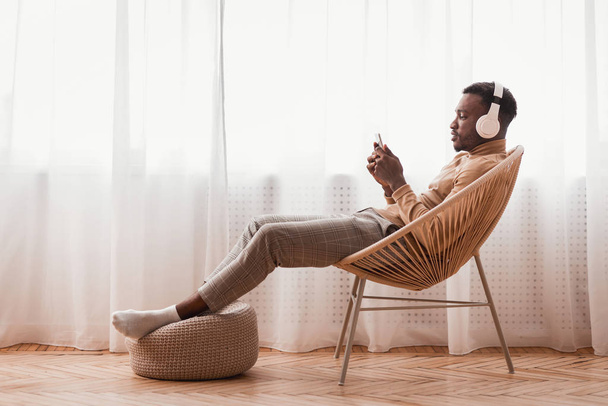 Millennial Afro Guy En Auriculares Usando Smartphone Sentado Interior
 - Foto, imagen