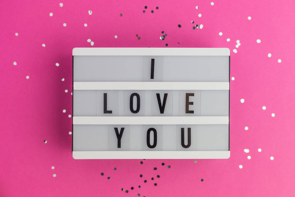 Ik hou van je tekst op witte lichtbak. Roze achtergrond met veelkleurige confetti. Vlakke lay stijl. Bovenaanzicht - Foto, afbeelding