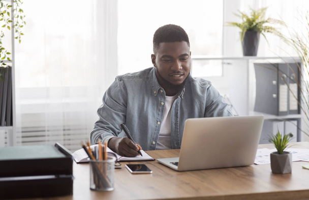 Jeune homme d'affaires utilisant un ordinateur portable et prenant des notes à la dentelle de travail dans le bureau
 - Photo, image