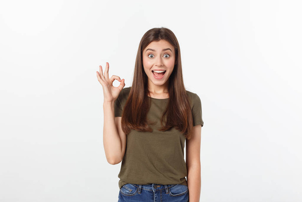 Happy young woman showing ok sign with fingers an winking isolated on a gray background. - Фото, изображение