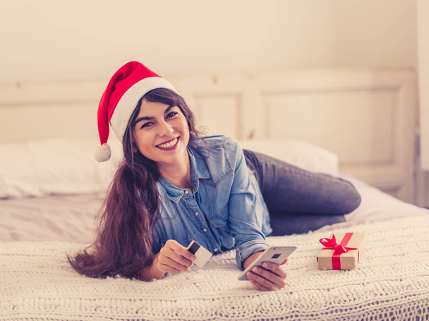 Γυναίκα στο καπέλο santa claus αγορά χριστουγεννιάτικα δώρα με κινητό τηλέφωνο και πιστωτική κάρτα ενθουσιασμένος για τις χειμερινές διακοπές. Ηλεκτρονικές πωλήσεις, Αγορές σε smartphone, e-Commerce μέσω κινητού και Καλά Χριστούγεννα. - Φωτογραφία, εικόνα