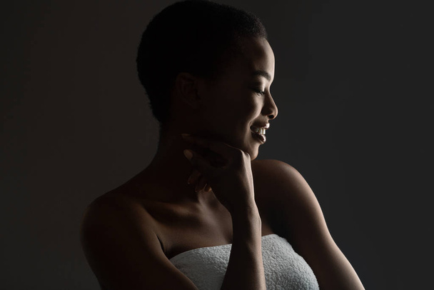 Portrait of beautiful african girl wrapped in towel, standing in darkness - Foto, Imagen