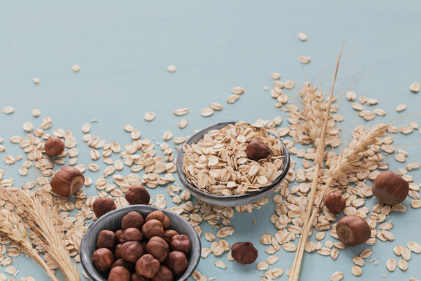 Dry oatmeal flakes with ears of wheat and hazelnuts on light gre - Foto, Bild