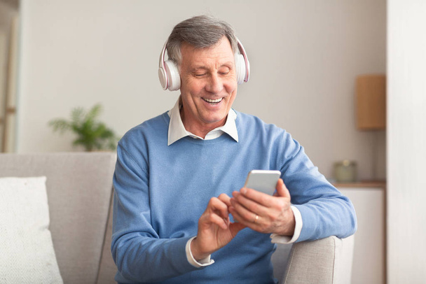Uomo anziano in ascolto di canzone utilizzando smartphone seduto sul divano
 - Foto, immagini