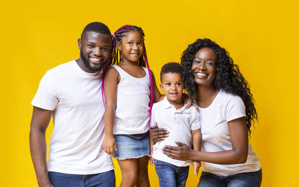 Улыбающиеся чёрные родители с двумя маленькими детьми на жёлтом фоне
 - Фото, изображение