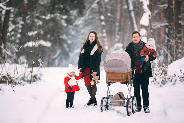 Een prachtig gezin met retro kinderwagen wandelt door het winterse besneeuwde bos. Moeder, vader, dochter en zoontje genieten van de dag buiten. Vakantie, kerst, samen gelukkig zijn, verliefd zijn op een kind. - Foto, afbeelding