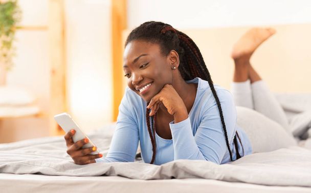 Menina negra usando Smartphone deitado na cama em casa
 - Foto, Imagem