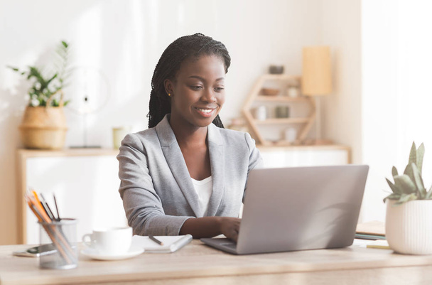 Lächelnde Afro-Geschäftsfrau arbeitet im modernen Büro am Laptop - Foto, Bild