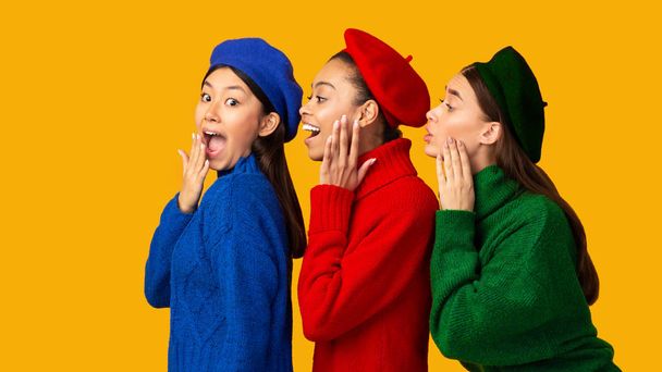 Три багатонаціональні дівчини - пліткарки шипіння секретів через жовте тло, панорама - Фото, зображення
