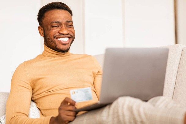 Hombre celebración de compras con tarjeta de crédito en línea usando el ordenador portátil en casa
 - Foto, imagen
