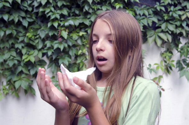 Dziewczynka kicha w chusteczce w zielonym parku. Dziewczynka ma alergię na pyłki lub grypę.. - Zdjęcie, obraz