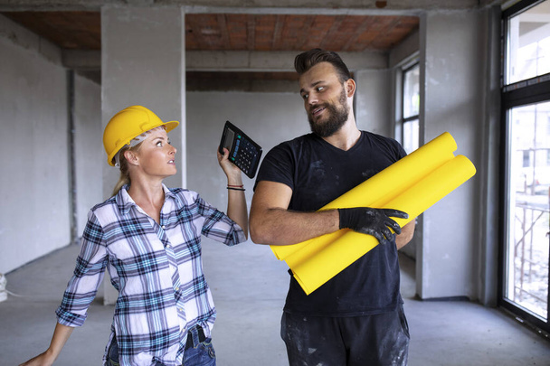 Woman and man civil engineer worker on construction site controlling architectural project plan talking about reconstruction business inside the building. Two builder people talking professional - Foto, Imagem