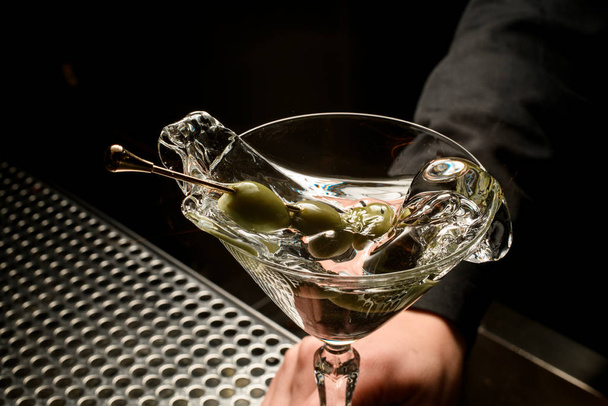 Vrouwelijke barman serveert transparante cocktail op basis van martini versierd met olijven op de prikker spetterend het - Foto, afbeelding