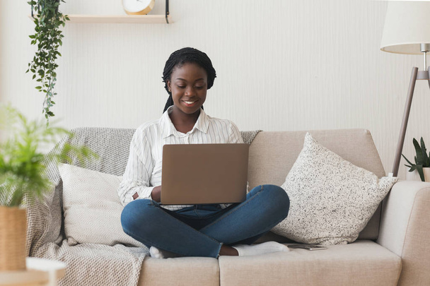 Mosolygó afrikai lány használ laptop számítógép kanapén otthon - Fotó, kép