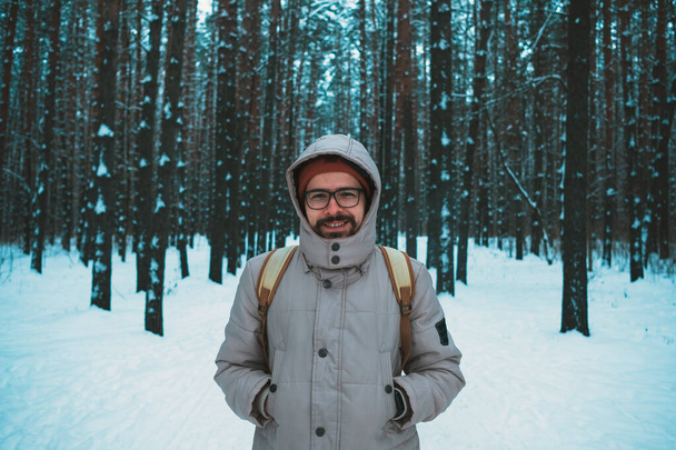 νεαρός άνδρας στέκεται στο χειμερινό χιονισμένο δάσος - Φωτογραφία, εικόνα
