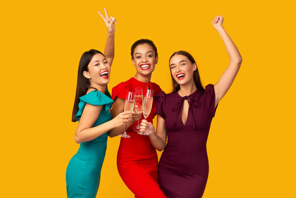 Three Models Clinking Glasses Having Fun Standing Over Yellow Background - Photo, image