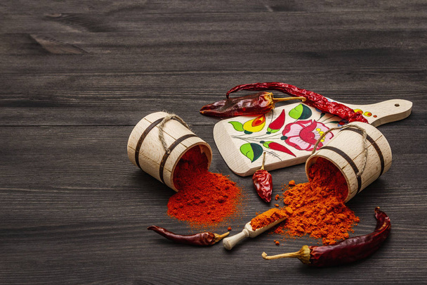 Magyar (Hungarian) red sweet and hot paprika powder. Traditional pattern on a cutting board, different varieties of dry pepper. Black wooden background - Photo, Image