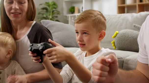 A boy with a gamepad plays video games with dad, mom and little brother - Video, Çekim